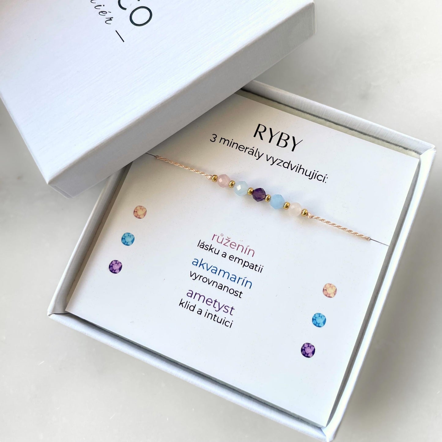 Bílá krabička, ve které je náramek vytvořený z hedvábného provázku a pěti minerály. Náramek je upevněn na promo kartičce s nápisem Ryby. Náramek je udělán na téma Znamení Zvěrokruhu. Karta také obsahuje vysvětlivky ke každému použitému kameni: Růženín pro Lásku a Empatii, Akvamarín pro Vyrovnanost, Ametyst pro Klid a Intuici
