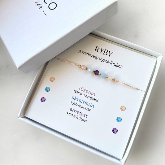 Bílá krabička, ve které je náramek vytvořený z hedvábného provázku a pěti minerály. Náramek je upevněn na promo kartičce s nápisem Ryby. Náramek je udělán na téma Znamení Zvěrokruhu. Karta také obsahuje vysvětlivky ke každému použitému kameni: Růženín pro Lásku a Empatii, Akvamarín pro Vyrovnanost, Ametyst pro Klid a Intuici