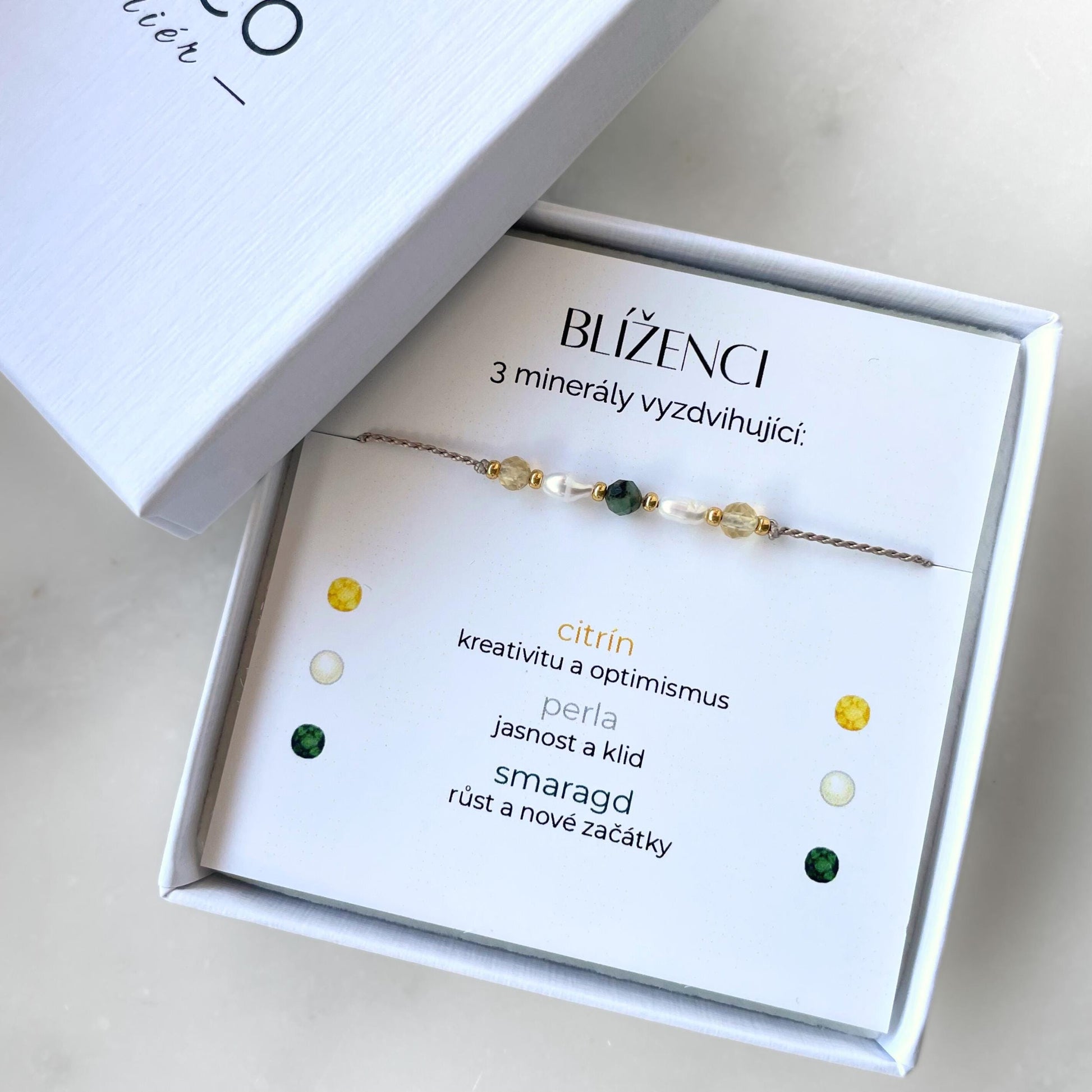 Bílá krabička, ve které je náramek vytvořený z hedvábného provázku a pěti minerály. Náramek je upevněn na promo kartičce s nápisem Blíženci. Náramek je udělán na téma Znamení Zvěrokruhu. Karta také obsahuje vysvětlivky ke každému použitému kameni: Citrín pro Kreativitu a Optimismus, Perla pro Jasnost a Klid, Smaragd pro Růst a Nové Začátky