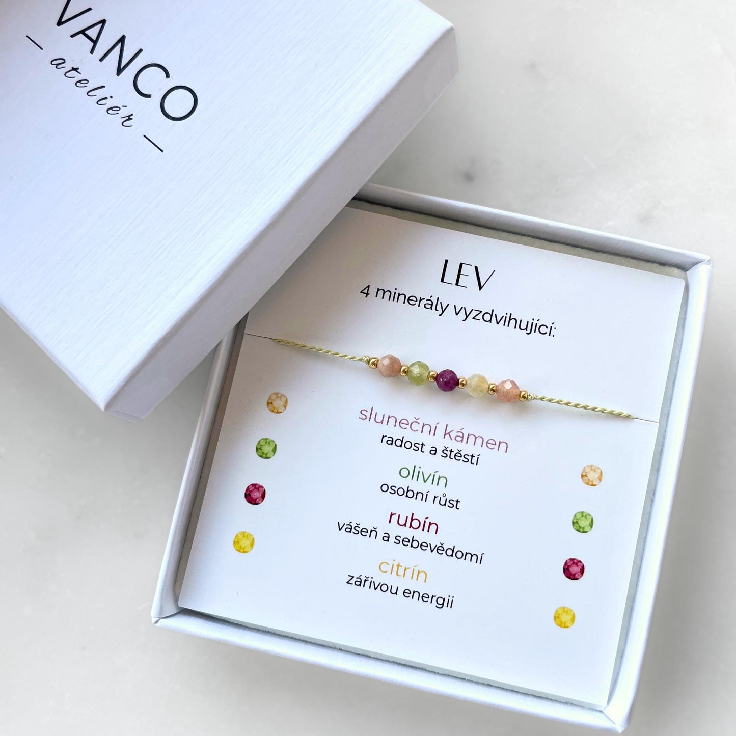 Bílá krabička, ve které je náramek vytvořený z hedvábného provázku a pěti minerály. Náramek je upevněn na promo kartičce s nápisem Lev. Náramek je udělán na téma Znamení Zvěrokruhu. Karta také obsahuje vysvětlivky ke každému použitému kameni: Sluneční Kámen pro Radost a Štěstí, Olivín pro Osobní Růst, Rubín pro Vášeň a Sebevědomí, Citrín pro Zářivou Energii