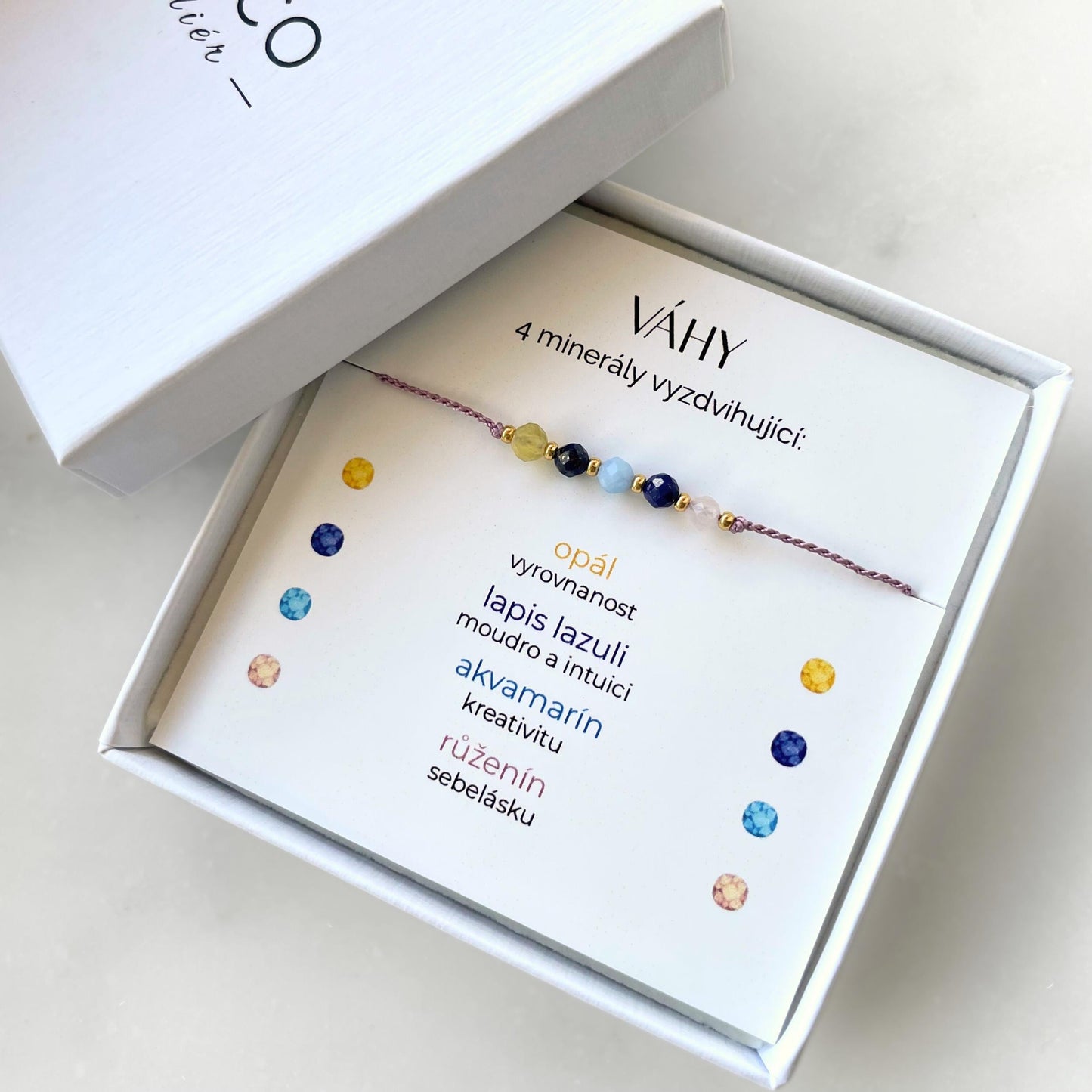 Bílá krabička, ve které je náramek vytvořený z hedvábného provázku a pěti minerály. Náramek je upevněn na promo kartičce s nápisem Váhy. Náramek je udělán na téma Znamení Zvěrokruhu. Karta také obsahuje vysvětlivky ke každému použitému kameni: Opál pro Vyrovnanost, Lapis Lazuli pro Moudro a Intuici, Akvamarín pro Kreativitu, Růženín pro Sebelásku