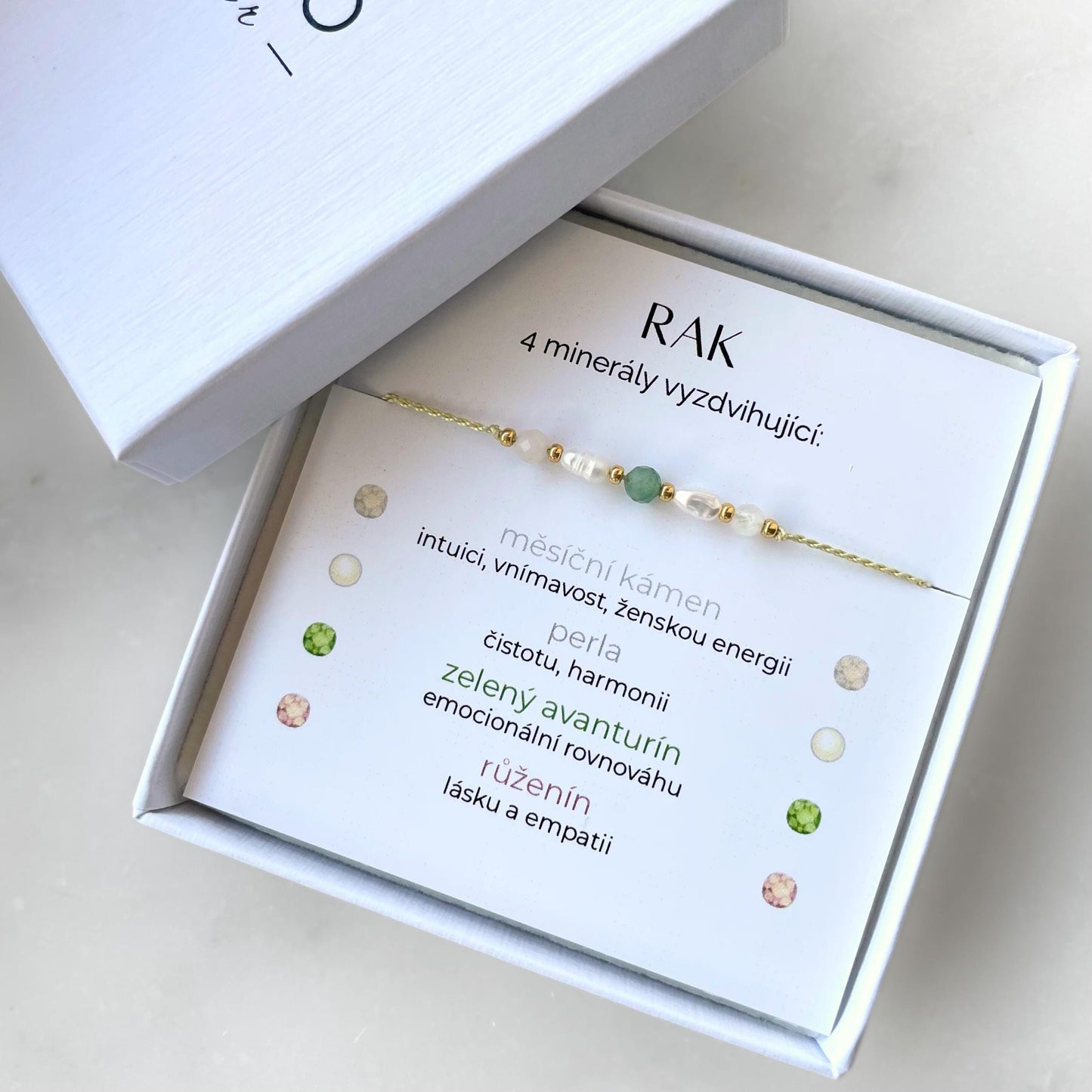 Bílá krabička, ve které je náramek vytvořený z hedvábného provázku a pěti minerály. Náramek je upevněn na promo kartičce s nápisem Rak. Náramek je udělán na téma Znamení Zvěrokruhu. Karta také obsahuje vysvětlivky ke každému použitému kameni: Měsíční Kámen pro Intuici, Vnímavost, Ženskou Energii; Perla pro Čistotu a Harmonii; Avanturín pro Emocionální Rovnováhu; Růženín pro Lásku a Empatii