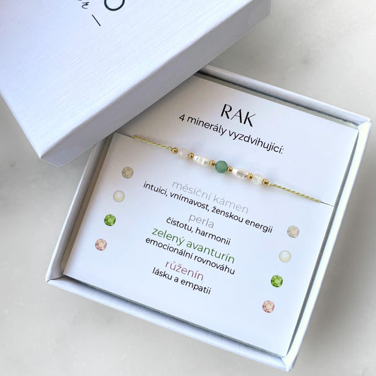 Bílá krabička, ve které je náramek vytvořený z hedvábného provázku a pěti minerály. Náramek je upevněn na promo kartičce s nápisem Rak. Náramek je udělán na téma Znamení Zvěrokruhu. Karta také obsahuje vysvětlivky ke každému použitému kameni: Měsíční Kámen pro Intuici, Vnímavost, Ženskou Energii; Perla pro Čistotu a Harmonii; Avanturín pro Emocionální Rovnováhu; Růženín pro Lásku a Empatii