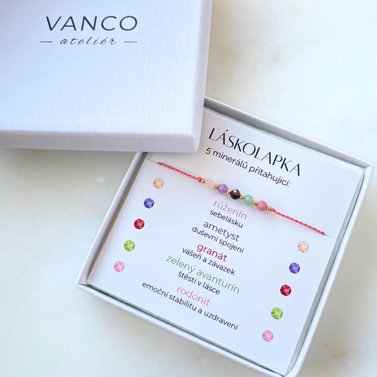Bílá krabička, ve které je náramek vytvořený z hedvábného provázku a pěti minerály. Náramek je upevněn na promo kartičce s nápisem Láskolapka. Náramek je udělán na téma Lásky. Karta také obsahuje vysvětlivky ke každému použitému kameni: Růženín pro Sebelásku, Ametyst pro Duševní Spojení, Granát pro Vášeň a Závazek, Zelený Avanturín pro Štěstí v Lásce, Rodonit pro Emoční Stabilitu a Uzdravení