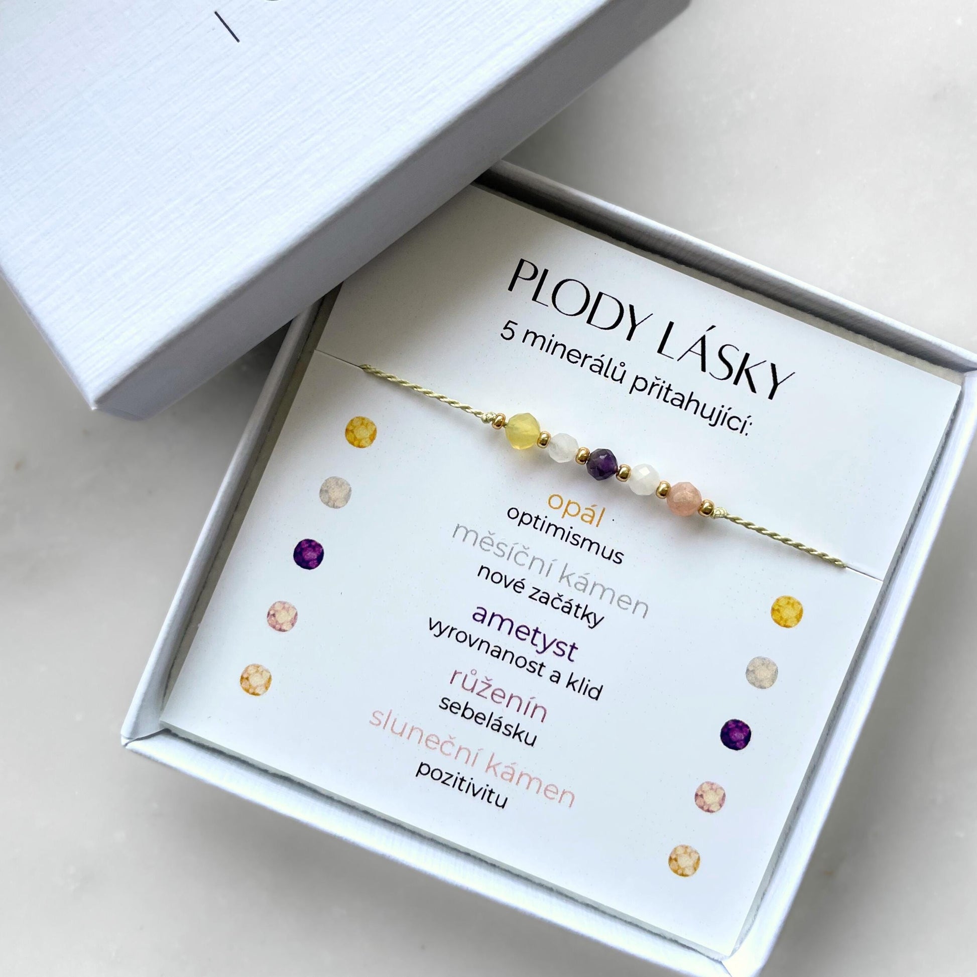 Bílá krabička, ve které je náramek vytvořený z hedvábného provázku a pěti minerály. Náramek je upevněn na promo kartičce s nápisem Plody Lásky. Náramek je udělán na téma Plodnost. Karta také obsahuje vysvětlivky ke každému použitému kameni: Opál pro Optimismus, Měsíční Kámen pro Nové Začátky, Ametyst pro Vyrovnanost a Klid, Růženín pro Sebelásku, Sluneční Kámen pro Pozitivitu