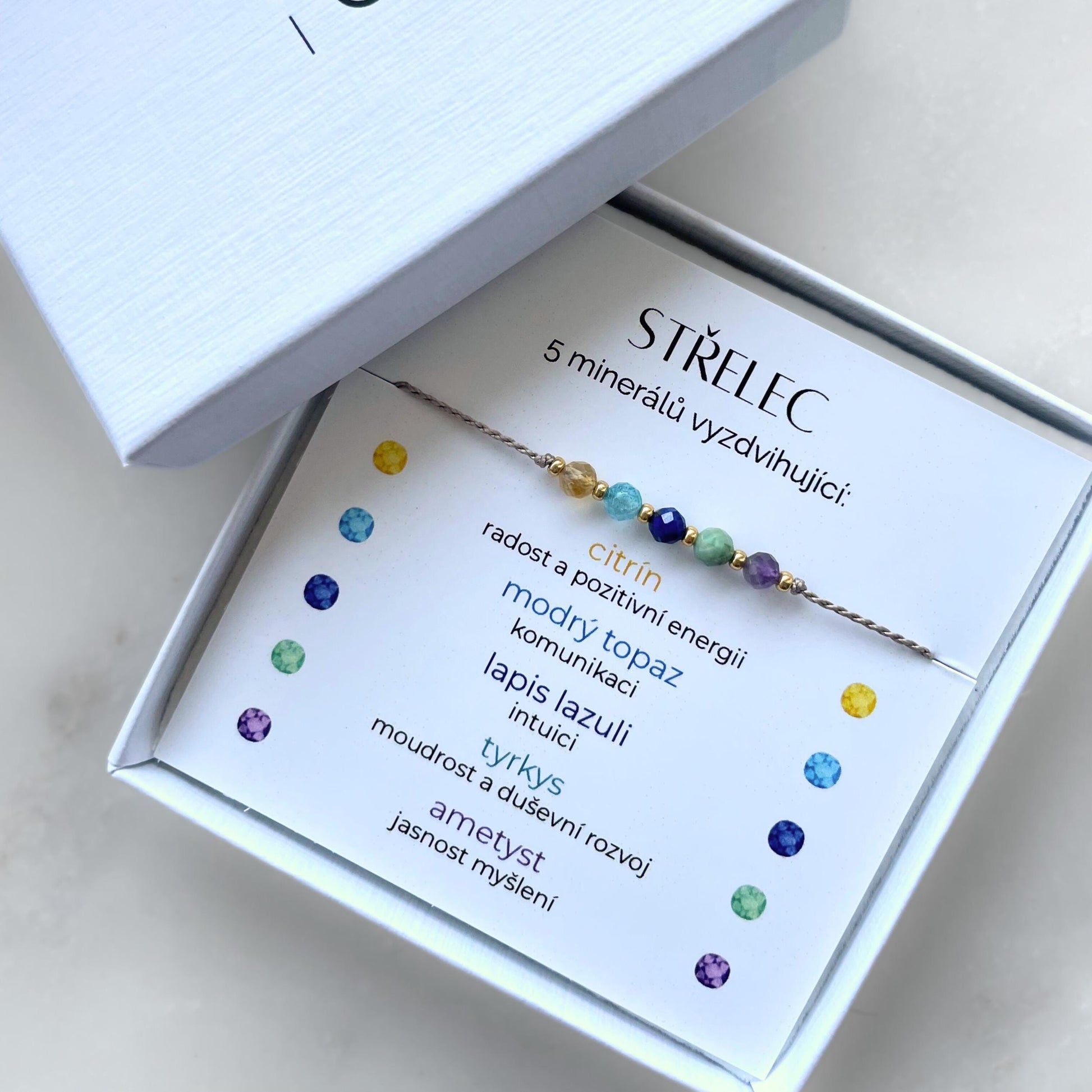Bílá krabička, ve které je náramek vytvořený z hedvábného provázku a pěti minerály. Náramek je upevněn na promo kartičce s nápisem Střelec. Náramek je udělán na téma znamení zvěrokruhu Střelec. Karta také obsahuje vysvětlivky ke každému použitému kameni: Citrín pro Radost a Pozitivní Energii, Modrý Topaz pro Komunikaci, Lapis Lazuli pro Intuici, Tyrkys pro Moudrost a Duševní Rozvoj, Ametyst pro Jasnost Myšlení