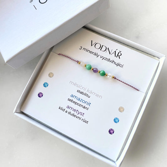 Bílá krabička, ve které je náramek vytvořený z hedvábného provázku a pěti minerály. Náramek je upevněn na promo kartičce s nápisem Vodnář. Náramek je udělán na téma Znamení Zvěrokruhu. Karta také obsahuje vysvětlivky ke každému použitému kameni: Měsíční Kámen pro Stabilitu, Amazonit pro Sebepoznání, Ametyst pro Klid a Duševní Růst