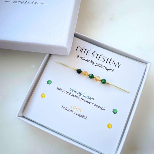 Bílá krabička, ve které je náramek vytvořený z hedvábného provázku a pěti minerály. Náramek je upevněn na promo kartičce s nápisem Dítě Štěstěny. Náramek je udělán na téma Štěstí. Karta také obsahuje vysvětlivky ke každému použitému kameni: Zelený Jadeit pro Štěstí, Bohatství a Pozitivní Energii, Citrín pro Hojnost a Úspěch