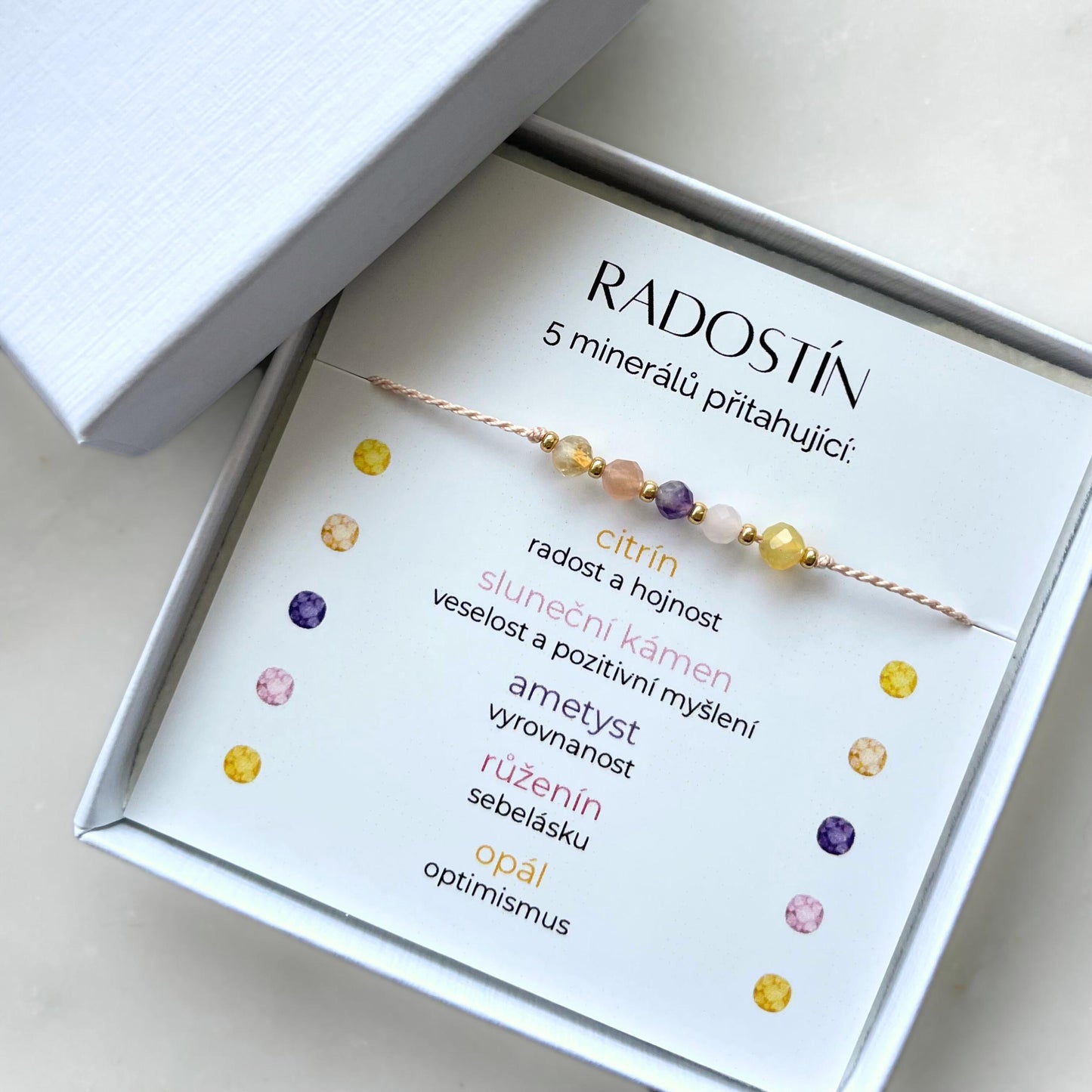 Bílá krabička, ve které je náramek vytvořený z hedvábného provázku a pěti minerály. Náramek je upevněn na promo kartičce s nápisem Radostín. Náramek je udělán na téma Radost. Karta také obsahuje vysvětlivky ke každému použitému kameni: Citrín pro Radost a Hojnost, Sluneční Kámen pro Veselost a Pozitivitu, Ametyst pro Vyrovnanost, Růženín pro Sebelásku, Opál pro Optimismus