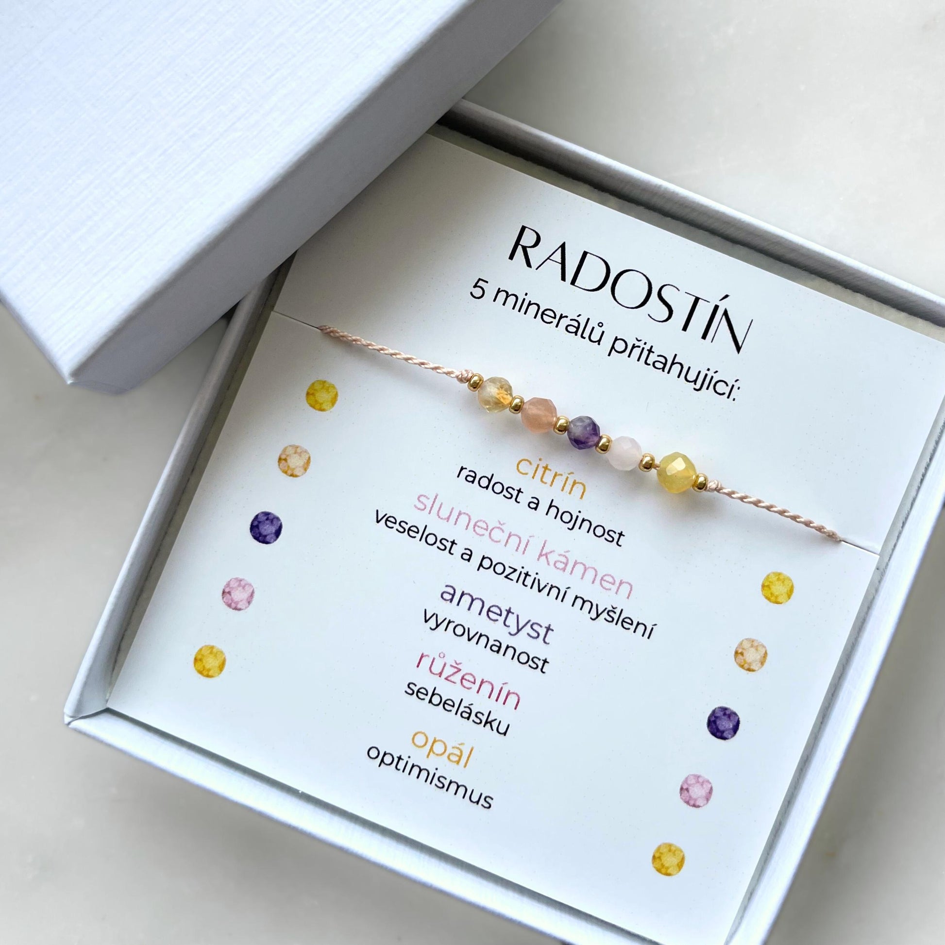 Bílá krabička, ve které je náramek vytvořený z hedvábného provázku a pěti minerály. Náramek je upevněn na promo kartičce s nápisem Radostín. Náramek je udělán na téma Radost. Karta také obsahuje vysvětlivky ke každému použitému kameni: Citrín pro Radost a Hojnost, Sluneční Kámen pro Veselost a Pozitivitu, Ametyst pro Vyrovnanost, Růženín pro Sebelásku, Opál pro Optimismus