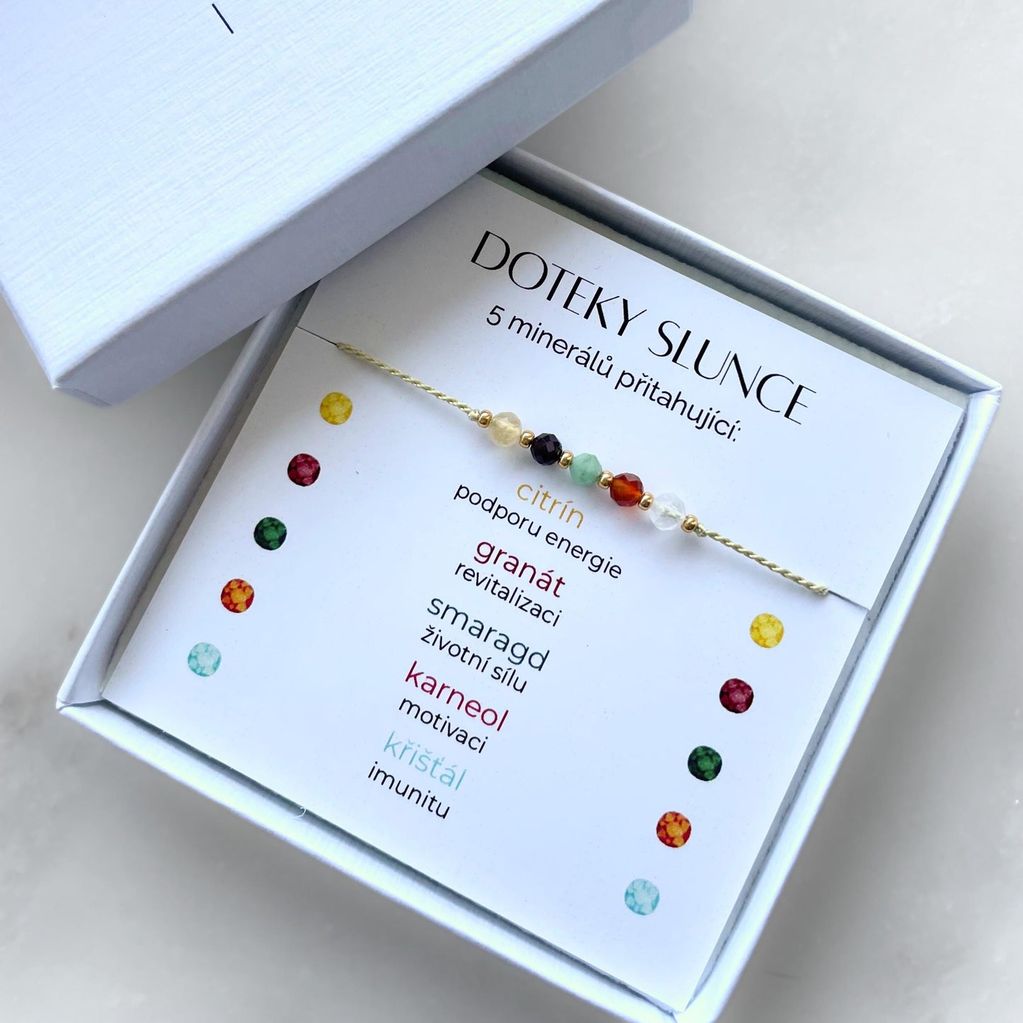 Bílá krabička, ve které je náramek vytvořený z hedvábného provázku a pěti minerály. Náramek je upevněn na promo kartičce s nápisem Doteky Slunce. Náramek je udělán na téma Vitalita. Karta také obsahuje vysvětlivky ke každému použitému kameni: Citrín pro Podporu Energie, Granát pro Revitalizaci, Smaragd pro Životní Sílu, Karneol pro Motivaci, Křišťál pro Imunitu