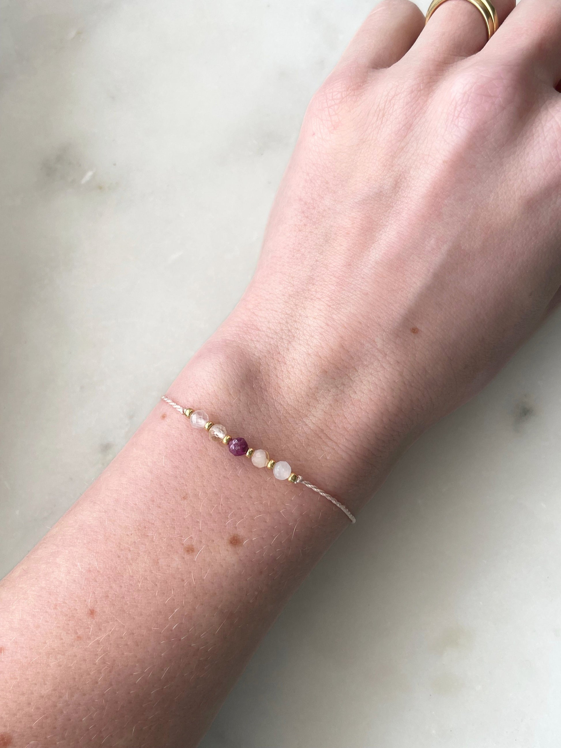 Růžový hedvábný náramek na ruce s pěti minerály: růženín, citrín, rubín, měsíční kámenl a zlaté korálky.